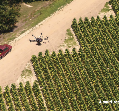 A multi-rotor drone hovering over crops